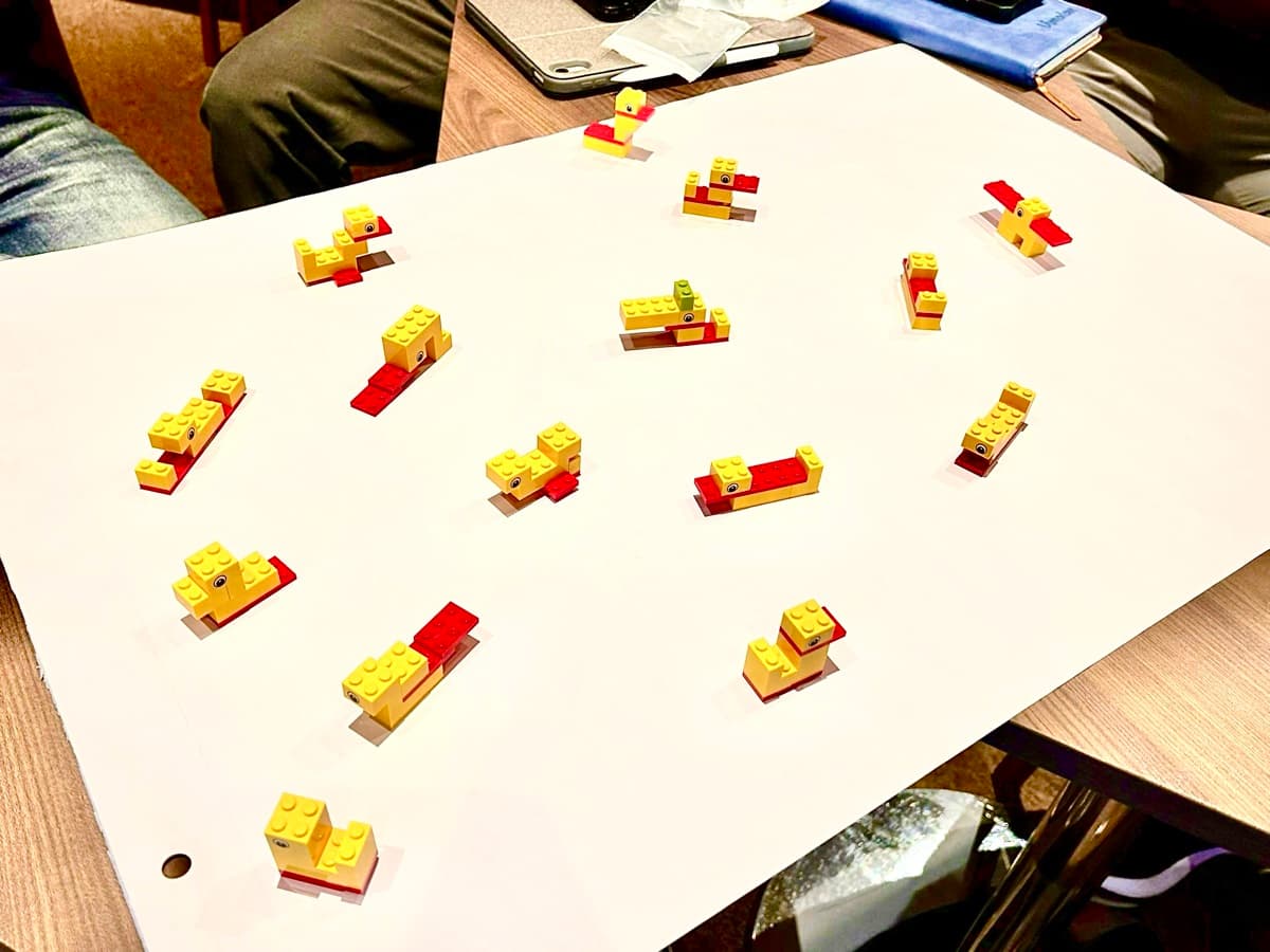 LEGO duck warm-up builds on a workshop table, the same bricks holding four different forms